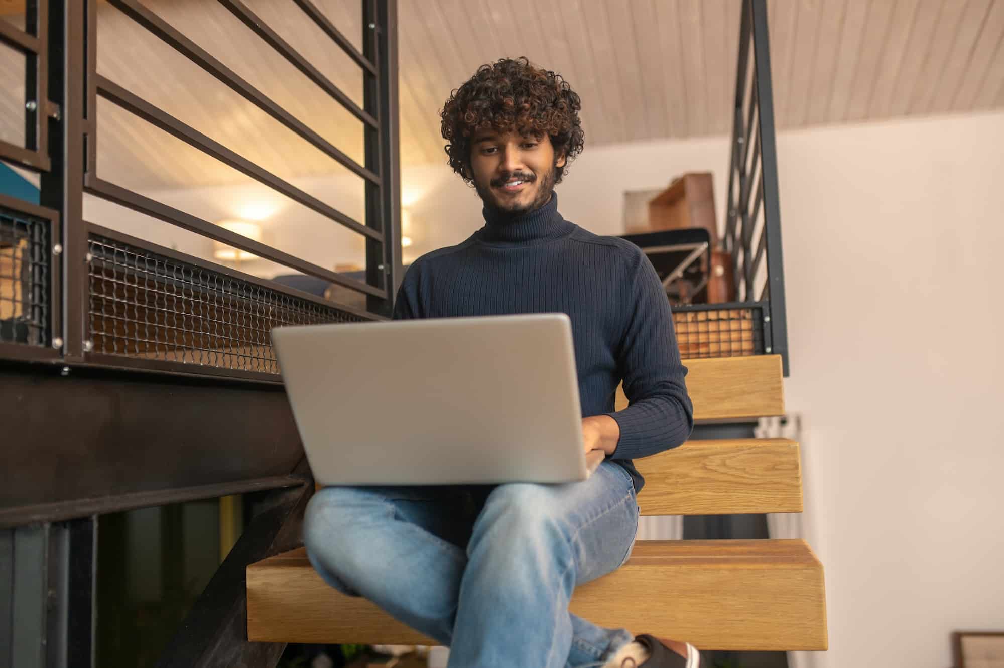 Man sitting on steps smiling looking at laptop