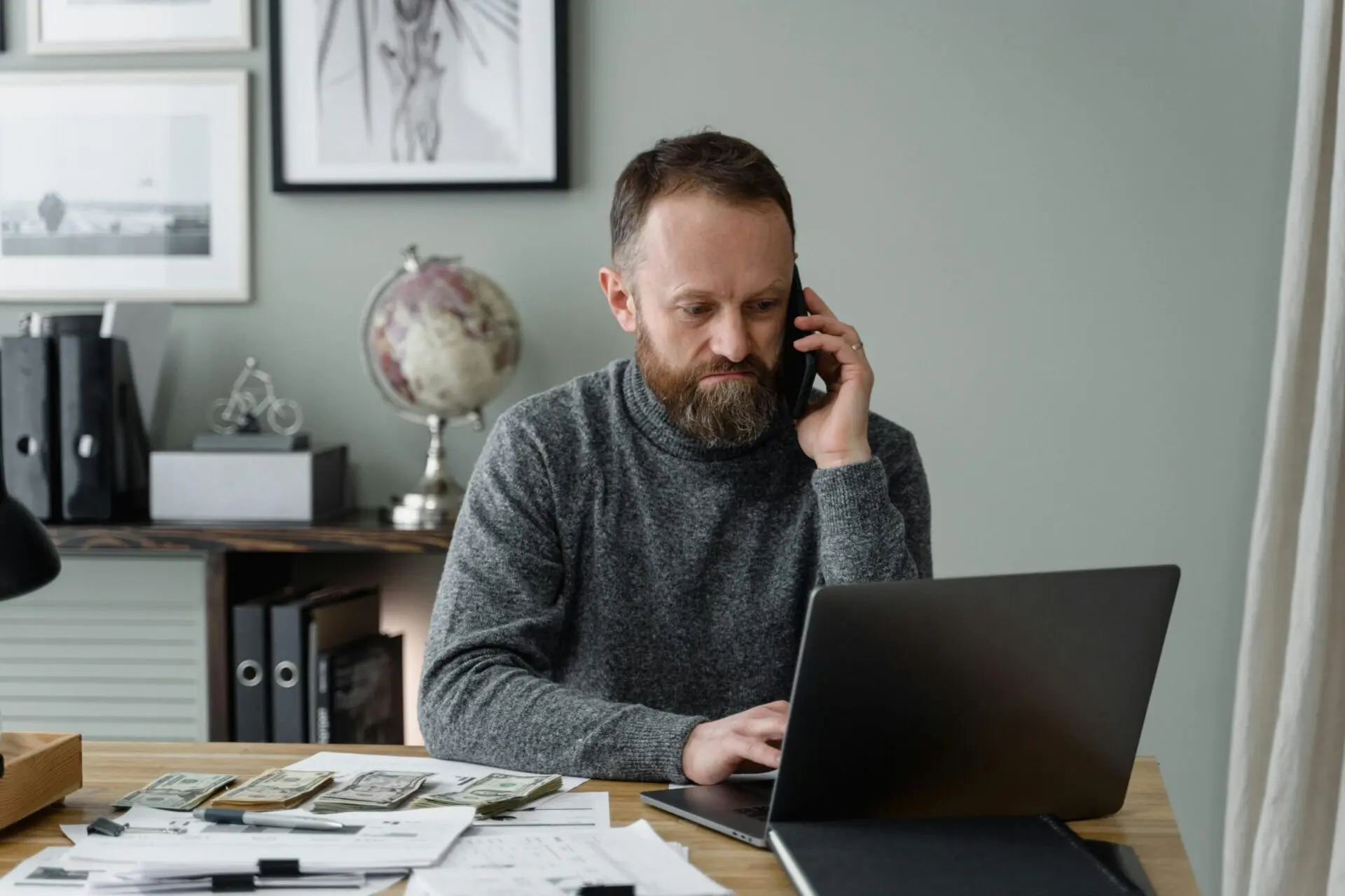 Professional consulting session with a man on the phone and working on a laptop with financial documents on his desk.