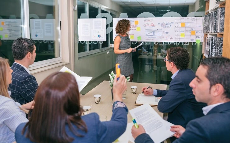 Change management workshop facilitator presenting to business team with process maps and sticky notes on glass board