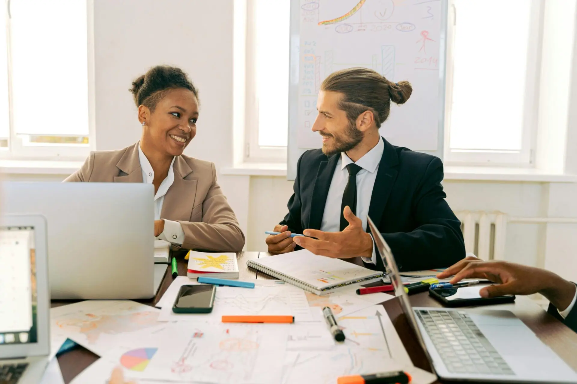 Digital brand consultancy professionals collaborating with laptops charts bright office