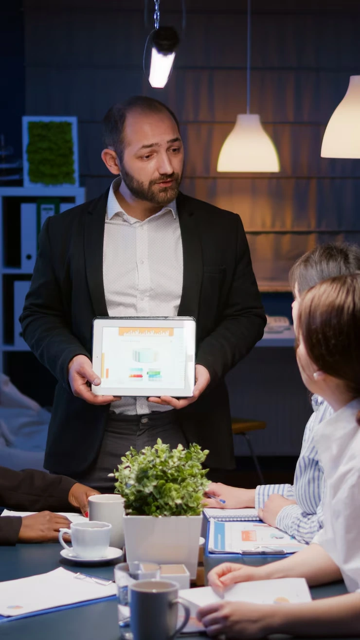 Professional consultant presenting data analytics on tablet to client in modern evening meeting