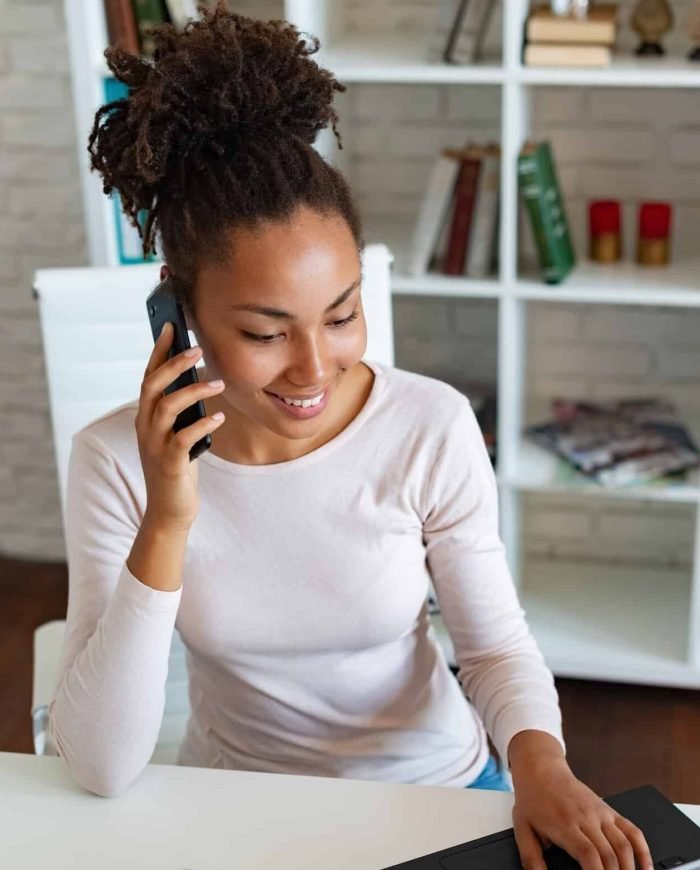 Smiling woman working on laptop in the office and talking on a smartphone . - Image