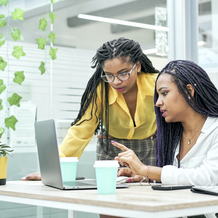 Two young black women reviewing analytical data on various electronic devices.