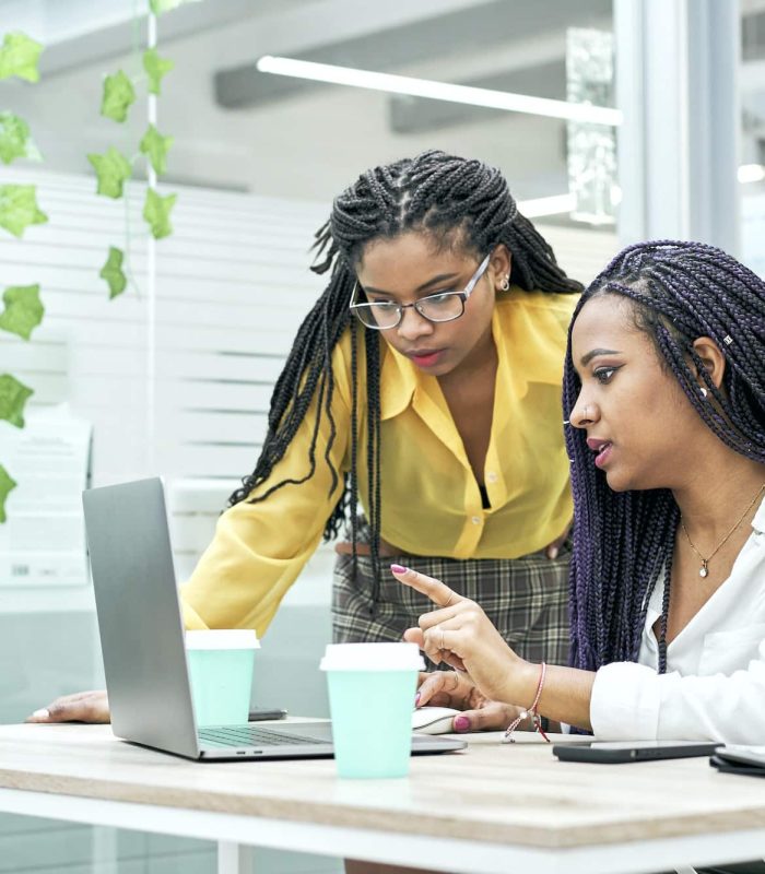 Two young black women reviewing analytical data on various electronic devices.